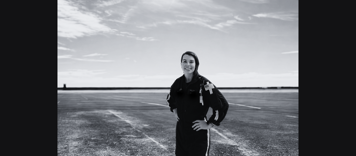 Black and white photo of a flight nurse standing on a flat, open landscape with a cloudy sky.