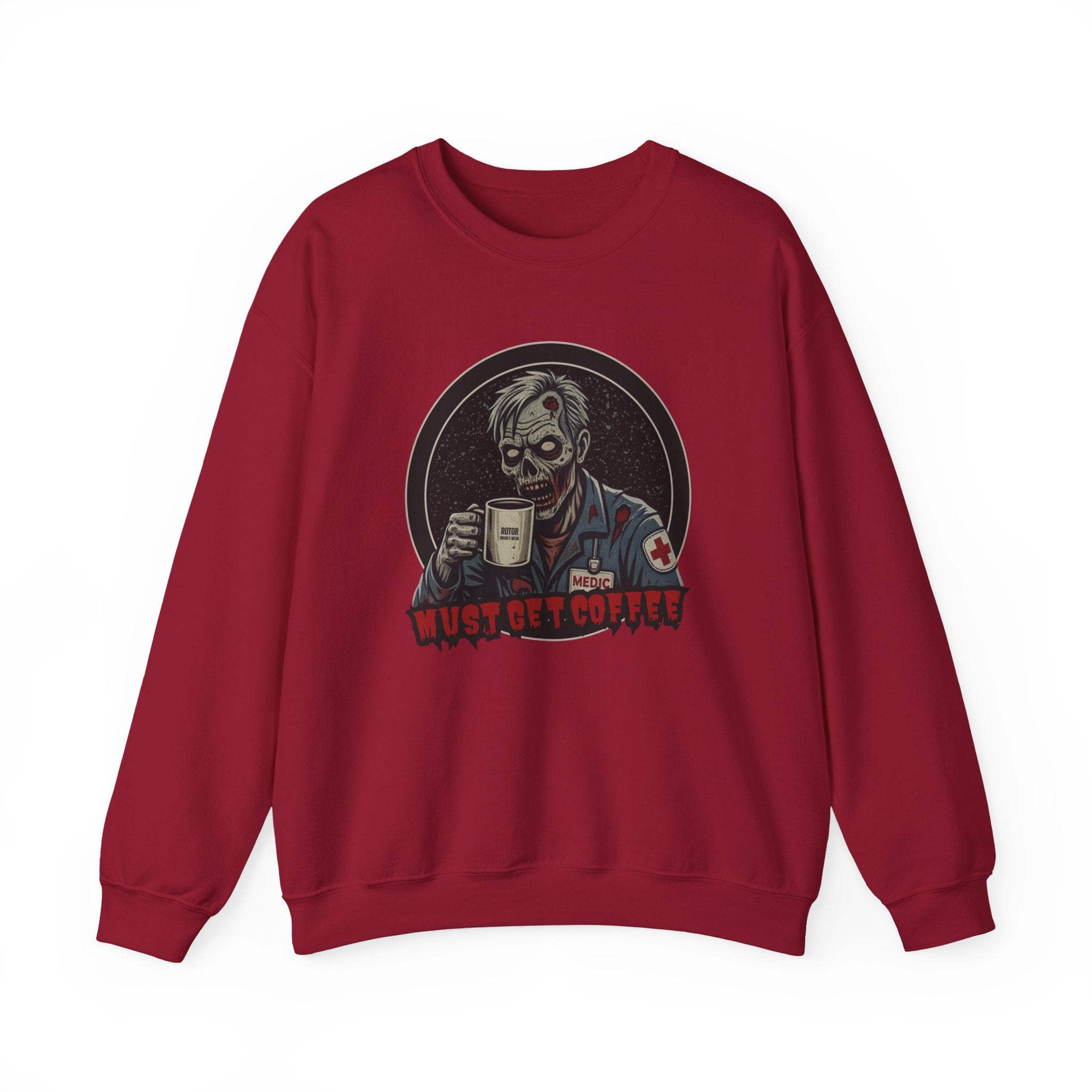 A red crewneck sweatshirt featuring a graphic print of a zombie in a medical uniform holding a coffee mug, with the text 'MUST GET COFFEE' below it by Rotor Wash & Wear