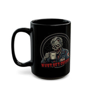 A black ceramic coffee mug featuring a zombie medic graphic holding a coffee mug, with the text 'MUST GET COFFEE' in red below by Rotor Wash & Wear