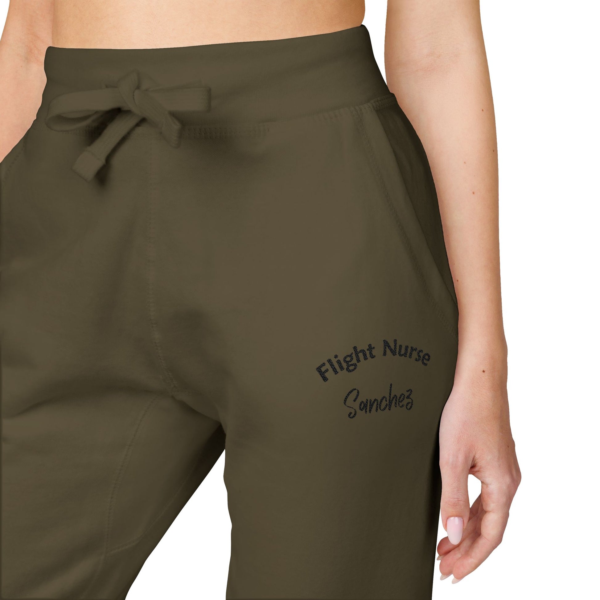 Olive green joggers with embroidered 'Flight Nurse Sanchez' text on the thigh against a white background