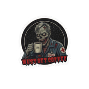 A die-cut vinyl sticker featuring a zombie dressed as a medic holding a coffee mug, with the text 'MUST GET COFFEE' in red at the bottom by Rotor Wash & Wear