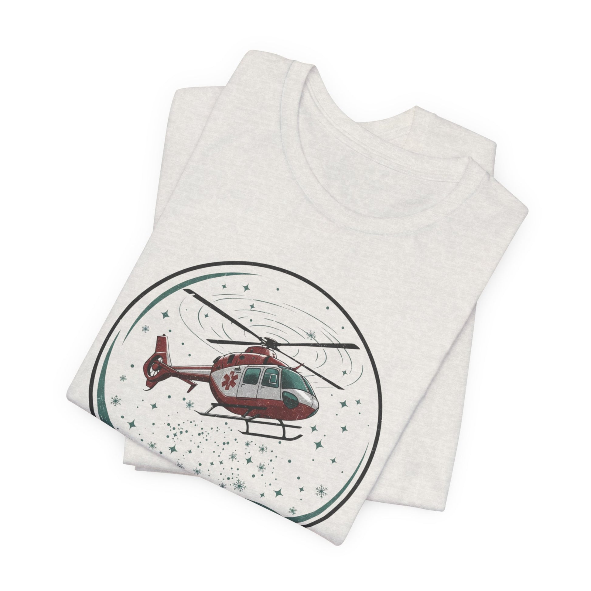 Folded heather cement t-shirt with a graphic of a helicopter in a snow globe and text "Heli-bells ring: certified for the holidays" by Rotor Wash & Wear
