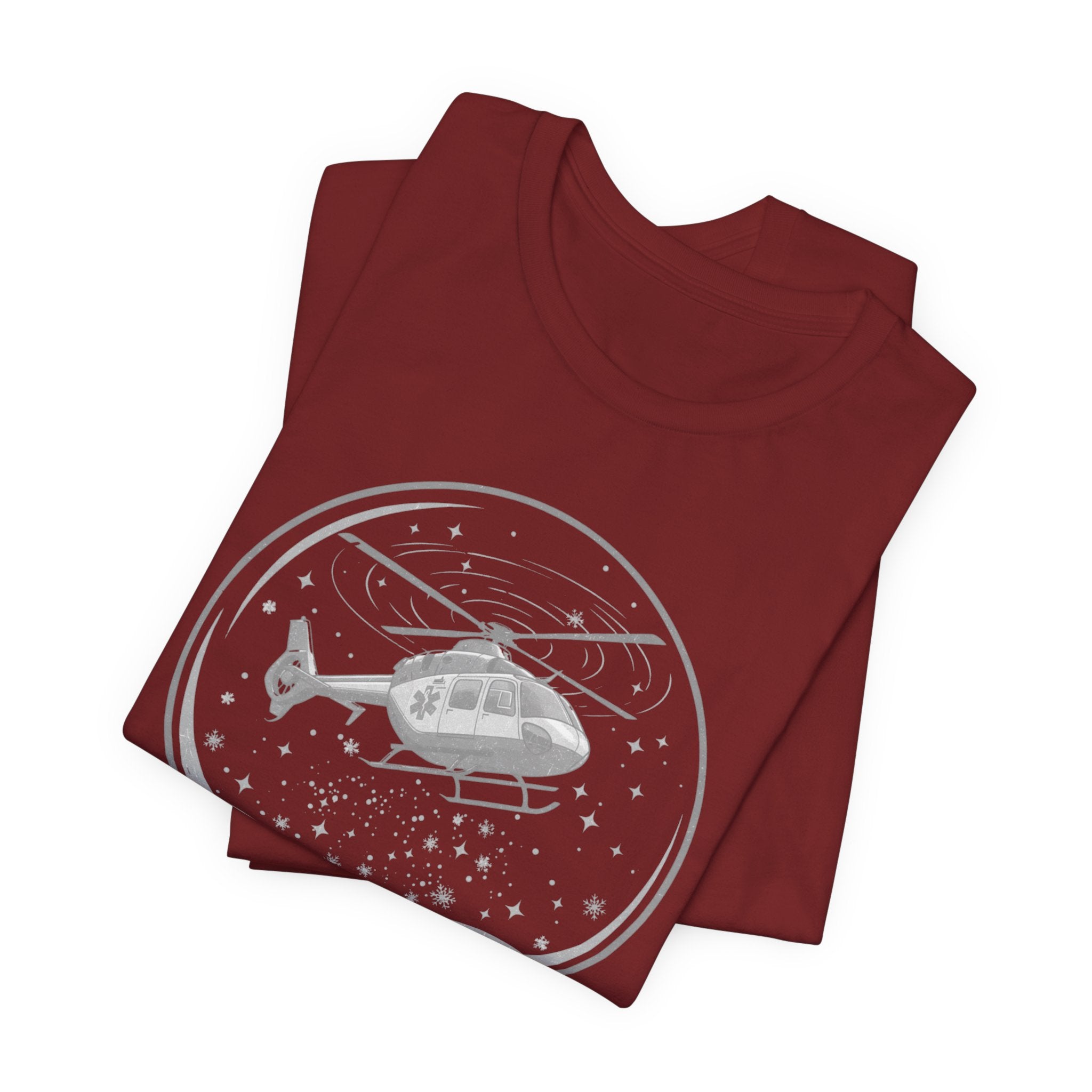Folded dark red t-shirt with a graphic of a helicopter in a snow globe and text "Heli-bells ring: certified for the holidays" by Rotor Wash & Wear