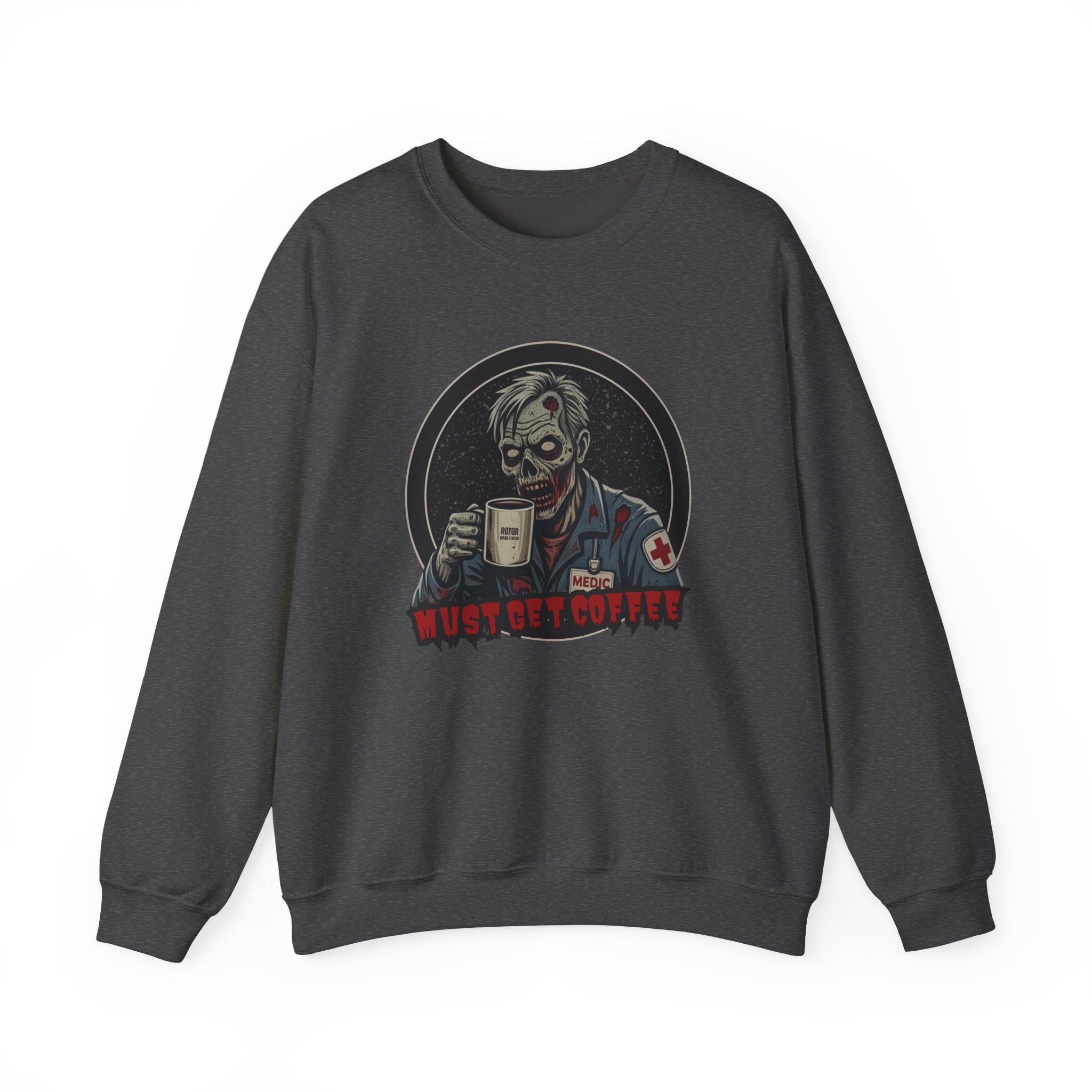 A dark gray heather crewneck sweatshirt featuring a graphic print of a zombie in a medical uniform holding a coffee mug, with the text 'MUST GET COFFEE' below it by Rotor Wash & Wear