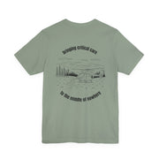 Sage green t-shirt with a helicopter graphic and text "bringing critical care to the middle of nowhere" on the back, displayed on a white background.