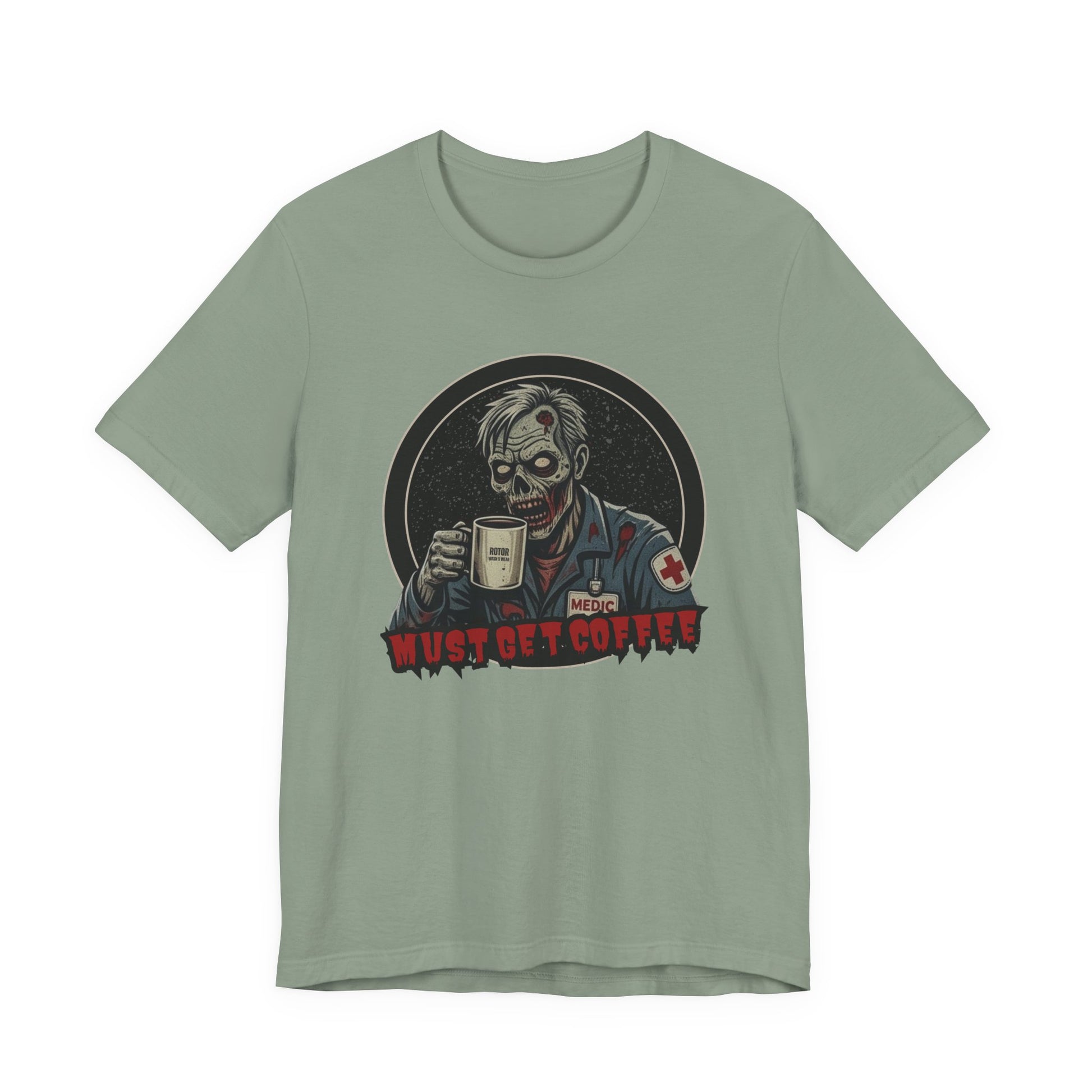 A sage green crewneck t-shirt featuring a graphic of a zombie medic holding a coffee mug with the text 'MUST GET COFFEE!' in red by Rotor Wash & Wear
